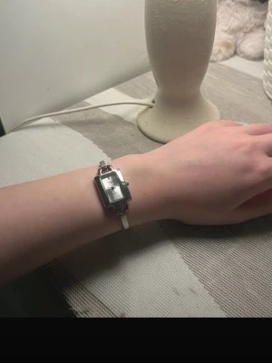 Rektangulär silverfärgad klocka - Stilren klocka med rektangulärt silverfärgat ur och vit rem. Urtavlan är enkel och klassisk med tydliga visare. Perfekt accessoar för dig som gillar minimalistisk design.