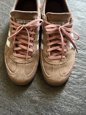 Adidas Spezial bruna sneakers - Säljer ett par Adidas Spezial sneakers i brunt mocka med ljusblå klassiska ränder på sidorna och rosa skosnören. Skorna har en låg profil och retroinspirerad design som passar perfekt till streetwear. Adidas-logga och Spezial-tryck på sidan. Storlek 40 2/3. 