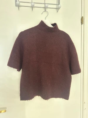 Brun stickad tröja med halv polo - Mysig brun stickad tröja med halv polokrage och korta ärmar. Tröjan har en rak passform och är gjord i ett mjukt, fluffigt material som känns skönt mot huden. Perfekt för lager på lager och enkel att styla till olika outfits.