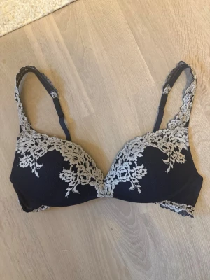 Mörkblå intimissmi bh - Snygg mörkblå bh med vadderade kupor och dekorativ vit spetsbrodyr framtill och längs axelbanden. Justerbara axelband och hakknäppning bak. Perfekt för dig som gillar romantiska detaljer och en feminin look. Pris kan diskuteras!