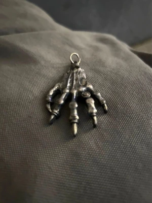 Hängsmycke skelett-hand i metall - Unikt hängsmycke i form av en skelett-hand, tillverkat i silverfärgad metall. Detaljerad design med tydliga leder och ben, perfekt för dig som gillar alternativa eller gotiska accessoarer. Passar till kedja eller band.