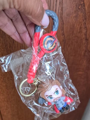 Nyckelring med Thor-figur Marvel - Säljer en cool nyckelring med en liten Thor-figur från Marvel. Nyckelringen har en flätad ögla i rött och grått samt en guldig ring. Thor-figuren är detaljerad med hammare, röd mantel och blå ögon. Perfekt för dig som gillar superhjältar!