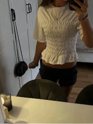 Vit smockad blus med volang - Säljer en söt vit croppad blus med korta ärmar och volangkant nedtill. Toppen har smockad midja som ger en snygg passform och en feminin look. Perfekt att matcha med shorts eller kjol för en fräsch stil. Jättefin till sommaren💓 Skriv för flera bilder💗 Accepterar inte under 130kr🫶🏻