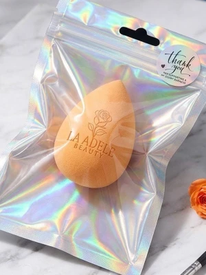 Persikofärgad beautyblender La Adele - En persikofärgad, droppformad beautyblender från La Adele Beauty. Perfekt för att applicera foundation och concealer jämnt. Tillverkad i mjukt, flexibelt skum som ger en naturlig finish. Kommer i en snygg, holografisk förpackning.