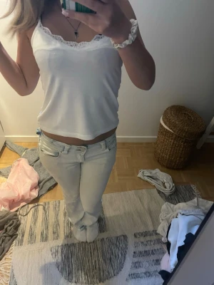 Ljusblå/vita low waist bootcut jeans - Säljer ett par ljusblå/vita low waist jeans med raka ben och klassisk femficksmodell. Jeansen har bälteshällor och stängs med knapp och dragkedja. Perfekta för dig som gillar en avslappnad och trendig look.
