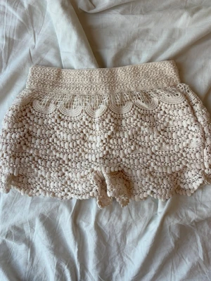 Beige virkade shorts från Gina Tricot - Säljer ett par superfina virkade shorts från Gina Tricot i beige. De har hög midja och ett detaljerat spetsmönster med volangkant upptill. Perfekta för sommarens alla tillfällen och riktigt sköna att bära. Katt finns i hemmet. Skriv om ni har frågor. 