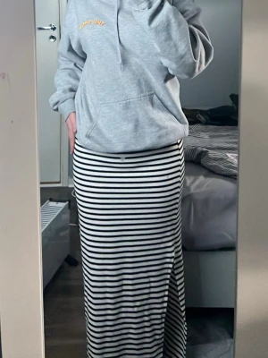 Randig långkjol med slits - Säljer en svartvit långkjol med horisontella ränder och slits på sidan. Kjolen har en tight passning och är perfekt för dig som gillar en enkel men snygg look. Materialet känns mjukt och stretchigt, troligen bomull eller polyester.
