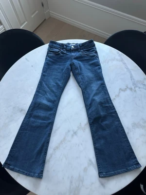 Blå bootcut jeans med låg midja - Snygga blå bootcut jeans med låg midja och klassisk femficksdesign. Jeansen har en lätt utsvängd passform.