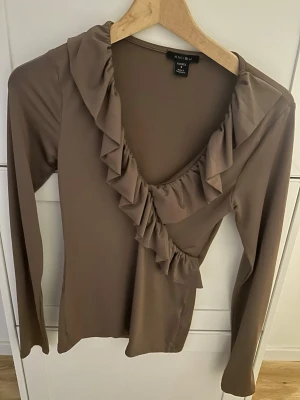 Brun volangtop från Amisu - Snygg brun långärmad topp från Amisu med djup V-ringning och volangdetaljer längs halsen och framtill. Tillverkad i ett mjukt, stretchigt material som sitter skönt på kroppen. Perfekt för dig som gillar feminina detaljer och en stilren look. Jättefin tröja använd 2 gånger men par inte på mig💕 