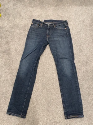 Mörkblå Levi's 511 jeans - Säljer ett par klassiska mörkblå jeans från Levi's med straight fit och fem fickor. Jeansen har snygga kontrastsömmar, läderpatch bak i midjan och är gjorda i slitstark denim. Perfekta för dig som gillar tidlös stil och vill ha ett par jeans som funkar till allt.