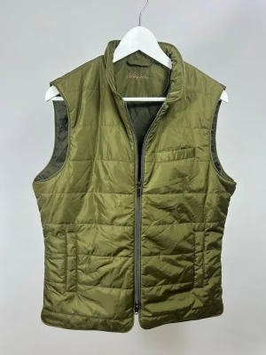 Stenströms Väst  - Snygg olivgrön väst från Stenströms med quiltad design och dragkedja framtill. Storlek M, modellen är 175 cm och väger 70 kg. Inga defekter, fint skick! Nylonmaterial. Västen har en stilren look med ståkrage och en bröstficka. 