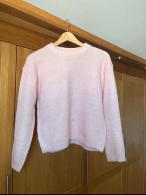 Ljusrosa stickad tröja från 157 - Mysig ljusrosa stickad tröja från 157 med rund halsringning och ribbade muddar. Tröjan har en enkel och clean design som passar perfekt till jeans eller kjol. Materialet känns mjukt och behagligt mot huden.