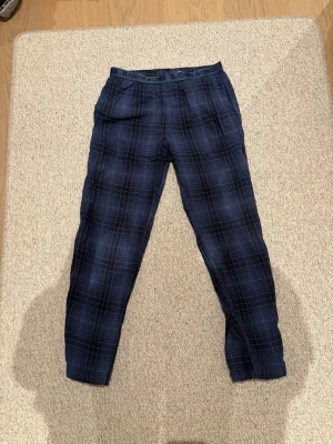 Mörkblå rutiga pyjamasbyxor Björn Borg - Snygga och bekväma mörkblå pyjamasbyxor från Björn Borg med rutigt mönster och resår i midjan med logga. Perfekta för chillkvällar hemma. Tillverkade i mjuk bomull för extra komfort.strl 158/164