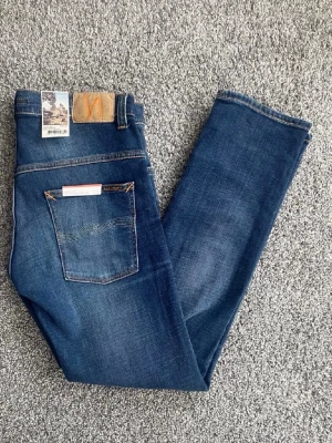  Helt nya Mörkblå jeans från Nudie Jeans - Snygga mörkblå jeans från Nudie Jeans med klassisk femficksmodell och subtila slitningar framtill. Jeansen har raka ben och kontrastsömmar samt en patch i läder bak i midjan. Perfekta för en avslappnad och trendig look.