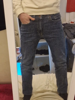 Blå slim fit jeans från Dressmann - Säljer ett par blå slim fit jeans från Dressmann med klassisk femficksdesign och snygga slitningar framtill. Jeansen har normal midja och raka ben, perfekta till vardagslooken. Materialet är mjukt denim i bomull med lite stretch för extra komfort.