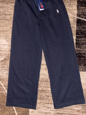 Mörkblå mjukisbyxor Polo Ralph Lauren - Säljer ett par mörkblå mjukisbyxor från Polo Ralph Lauren med dragsko i midjan och det klassiska vita logobroderiet på benet. Byxorna har raka ben och är tillverkade i mjukt bomullsmaterial för maximal komfort. Perfekta för chill dagar eller när du vill vara extra bekväm.