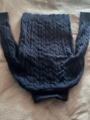 Mörkblå kabelstickad tröja Polo Ralph Lauren - Mörkblå kabelstickad tröja från Polo Ralph Lauren med halv dragkedja och hög krage. Tröjan har ett rött broderat logotyp på bröstet och ribbade muddar vid ärmslut och nederkant. Klassisk och tidlös design i mjukt material.