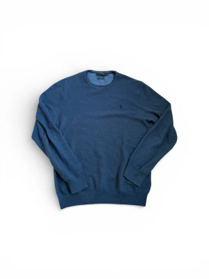 Blå stickad tröja från Polo Ralph Lauren - Mysig blå stickad tröja från Polo Ralph Lauren med rund halsringning och diskret broderad logga på bröstet. Tröjan har ribbade muddar vid ärmslut och nederkant och är tillverkad i mjukt material som passar perfekt till lager på lager.