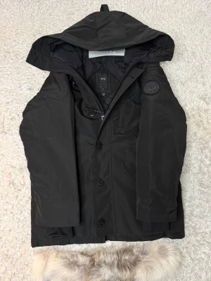 Canada Goose jacka  - Snygg svart dunjacka från Canada Goose med avtagbar huva och pälsdetalj. Jackan Är storlek S passar även M Riktig skön jacka säljer på grund av jag behöver inte den Bilderna är från när jag köpte den men den ser exakt lika ut fortfarande 