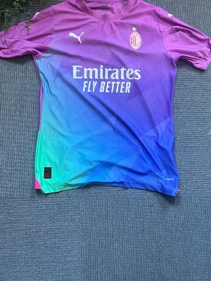 AC Milan x Puma färgglad matchtröja - Säljer en AC Milan matchtröja från Puma i en riktigt färgstark gradient från lila till blå och grön. Tröjan har korta ärmar, klubbmärke och Puma-logga på bröstet samt Emirates Fly Better-tryck. Tillverkad i lätt och ventilerande funktionsmaterial.