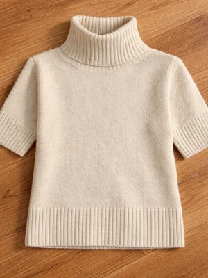 Beige stickad polotröja kort ärm - Snygg beige stickad polotröja med korta ärmar och bred ribbad kant vid hals, ärmslut och nederkant. Tröjan har en hög polokrage och är gjord i mjukt material, perfekt för lager på lager och en clean look.