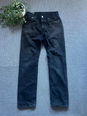 Svarta Levi's Premium raka jeans - Säljer ett par svarta Levi's Premium jeans i storlek W 30 L 32, med rak passform och klassisk femficksdesign. Jeansen har silverfärgade nitar och knapp, samt diskreta sömmar. Perfekta för dig som gillar en clean och tidlös look.