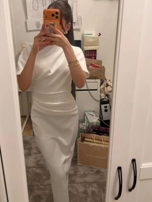 Vit långklänning med korta ärmar - Vit långklänning med korta ärmar och figurnära passform. Klänningen har en enkel och stilren design med hög hals och slät yta. 