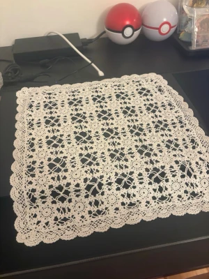 Virkad duk i vitt spetsmönster - Säljer en fyrkantig virkad duk i vitt med detaljerat spetsmönster och vågig kant. Perfekt som dekoration på bord eller byrå. Duken har ett klassiskt och elegant utseende med blommiga inslag i mönstret.
