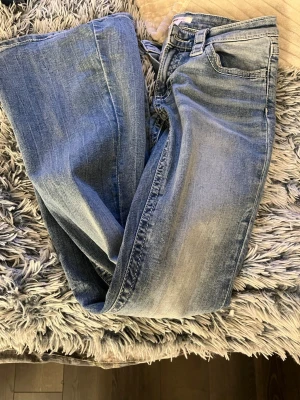 Blå bootcut jeans - Säljer ett par blå bootcut jeans med snygga tvättade detaljer. Jeansen har klassiska fem fickor och dekorativa sömmar på bakfickorna. Perfekta för dig som gillar en avslappnad och trendig stil. Storlek S från Gina Young. Knappt använda