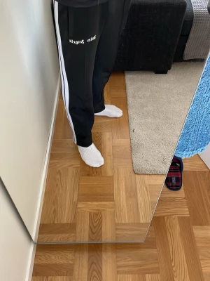 Palm Angels svarta - Säljer ett par svarta byxor från Palm Angels med vita sidoränder och logga framtill. Byxorna har rak passform, resår i midjan och är tillverkade i ett mjukt, stretchigt material som passar perfekt för chill dagar.