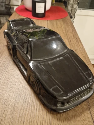 Svart keramikbil prydnad - Cool prydnad i form av en sportbil, tillverkad i svart keramik med blanka ytor. Bilen har detaljerade former som framhäver sportbilskänslan och passar perfekt som dekoration i hyllan eller på skrivbordet. Längd  43 cm. Bredd 15,5 cm. Se lilla skadan.