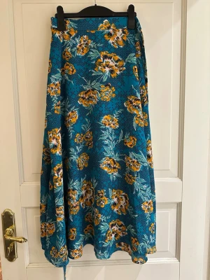 Kjol omlott blommig blå gul strl 36 - Säljer en långkjol med blommigt mönster i blått, gult.  Kjolen är tillverkad i 100% polyester. Omlottmodell, 