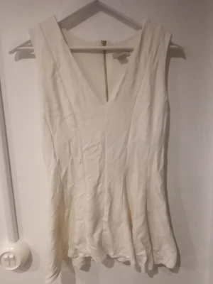 Vit ärmlös topp från H&M - Säljer en stilren vit klänning från H&M i storlek M. Klänningen är ärmlös med djup v-ringning och lätt utställd nederdel. Perfekt för sommardagar eller när du vill ha en enkel men snygg look.