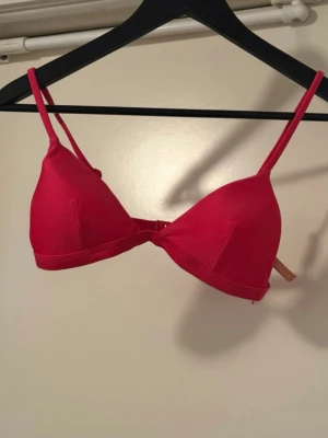 Rosa bikini överdel - Säljer en snygg röd bh med trekantskupor och justerbara axelband. Bh:n har en enkel design utan vaddering och stängs med hakar bak. 