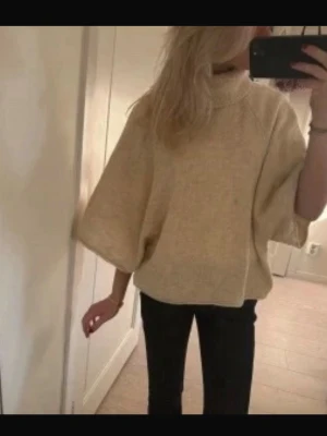 Stickad Beige bolero Zara  - Säljer en beige oversized stickad tröja med hög krage och vida trekvartsärmar. Tröjan har en avslappnad passform och är perfekt för lager på lager. Materialet ser mjukt och mysigt ut, perfekt för kyligare dagar.
