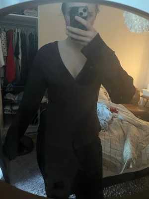 Svart omlottopp med v-ringning - Snygg svart omlottopp med djup v-ringning och långa ärmar. Toppen har en figurnära passform och är perfekt för att styla med både jeans och kjol. Materialet känns mjukt och följsamt mot kroppen.