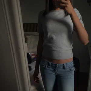 Ljusgrå stickad topp kort ärm - Ljusgrå stickad topp med korta ärmar och ribbad midja. Materialet ser ut att vara mjuk bomull eller bomullsblandning. Hålen är knappt synliga när man har på sig det 