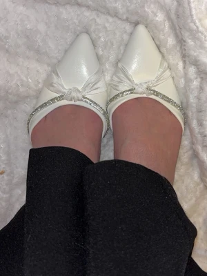 Vita spetsiga klackskor med glitter - Säljer nu mina helt nya vita klackskor. De är oanvända på grund av fel storlek. De har en ca 4 cm klack, vit knut och glitterdetalj framtill. 