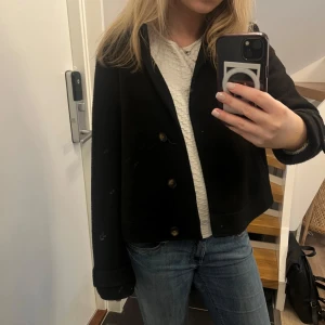 Kort kappa - Säljer en svart, kort kappa med klassisk krage och knäppning framtill. Står storlek medium men jag tycker den sitter mer som s/xs. Kappan har en rak passform och perfekt för en snygg look. Hör av dig om du har frågor.💗 den är lite nopprig