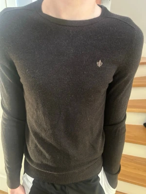 Mörkbrun stickad tröja Morris - Snygg mörkgrå stickad tröja från Morris med rund halsringning och diskret logga broderad på bröstet. Tröjan har långa ärmar och ribbade muddar vid ärmslut och nederkant. Perfekt till höst och vinter för en stilren look.