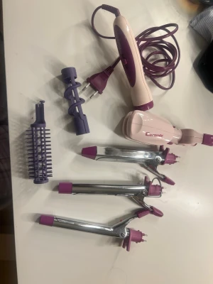 BaByliss multistyler rosa/lila - BaByliss multistyler i rosa och lila med flera utbytbara tillbehör, inklusive locktänger i olika storlekar, borste och spiralformad del. Perfekt för att skapa olika frisyrer. Elektrisk med keramisk beläggning och sladd. Plattong och fofeltång är i den lilla fyrkantiga huvudet genom att dra ner pil på sidan får du en platttång medan när du drar up samma pil blir det en vofeltång.