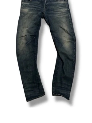 Mörkblå slitna jeans med tvättade detaljer - Säljer ett par mörkblå jeans med snygga slitningar och tvättade detaljer. Jeansen har rak passform och klassisk femficksdesign. Perfekta för en avslappnad och trendig look.