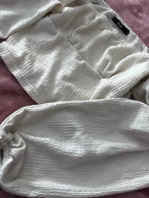 Vita crinkle-shorts från Bik Bok - Säljer en par vit topp från Bik Bok i storlek S. De har en crinkle-effekt i tyget, och är tillverkade i ett mjukt material som känns skönt mot huden. Perfekta för varma dagar oanvänd. 