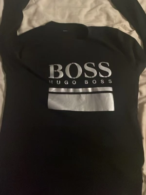 Hugo boss - Snygg svart sweatshirt från Hugo Boss med stort vitt logotryck på bröstet. Tröjan har rund halsringning och långa ärmar. Perfekt för en clean och stilren look.