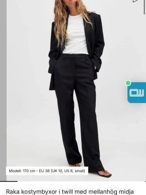 Raka kostymbyxor  - Snygga svarta kostymbyxor med rak passform och mellanhög midja. Byxorna är tillverkade i twilltyg och har klassisk design med hällor och fickor. Perfekta för en stilren look.