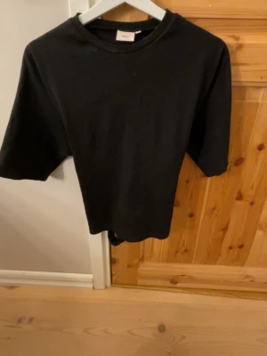 Svart t-shirt från Nelly - En stilren svart t-shirt från Nelly med klassisk rund halsringning och korta ärmar. Så fint att man kan knyta där bak till en rosett. T-shirten är i storlek s, pris kan diskuteras💗