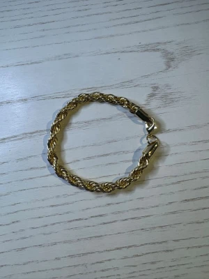 Guldigt tvinnat armband - Snyggt armband i guldfärgad metall med tvinnad design och robust lås. Perfekt för dig som vill ha en stilren och trendig accessoar som sticker ut. Armbandet har en klassisk look och passar till många olika outfits.