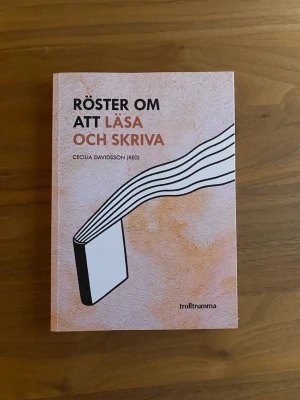 Röster om att läsa och skriva - Boken 'Röster om att läsa och skriva' är en samling essäer redigerad av Cecilia Davidsson. Omslaget är ljusrosa med grafisk illustration av en bok och svarta linjer. Perfekt för dig som gillar litteratur och skrivande.