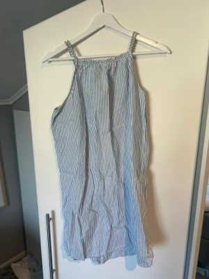 Blåvit randig sommarklänning - Säljer en luftig blåvit randig klänning med smala axelband och rak passform. Perfekt för varma dagar och enkel att styla med sneakers eller sandaler. Tillverkad i bomull för en skön känsla.