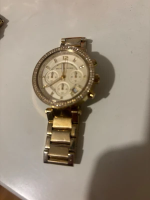 Äkta Guldig klocka från Michael Kors - Äkta Stilren guldig klocka från Michael Kors med länkarmband i metall och glittrande stenar runt urtavlan. Dam klocka, skriv vid frågor eller fler bilder. Pris går att pruta såklart 